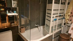 Une salle de bain avec une douche à parois de verre, un lavabo blanc avec des articles de toilette et un porte-serviettes avec des serviettes.