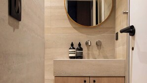 A modern bathroom with a wooden vanity, a round mirror, and a wall-mounted light fixture. - Charming Modern Studio With AC - Le Marais (Paris)