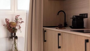 A modern kitchen with wooden cabinets, a black microwave, a coffee machine, and a vase with dried flowers on a round wooden table. - Charming Modern Studio With AC - Le Marais (Paris)