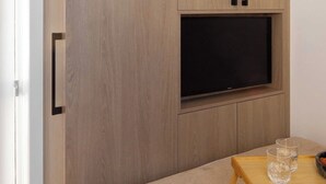 A bedroom with a bed, a TV mounted on a wooden cabinet, and a small wooden table with glasses. - Charming Modern Studio With AC - Le Marais (Paris)