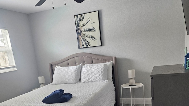Ein Schlafzimmer mit Bett, Deckenventilator, Nachttisch, Lampe und einem kleinen Tisch.