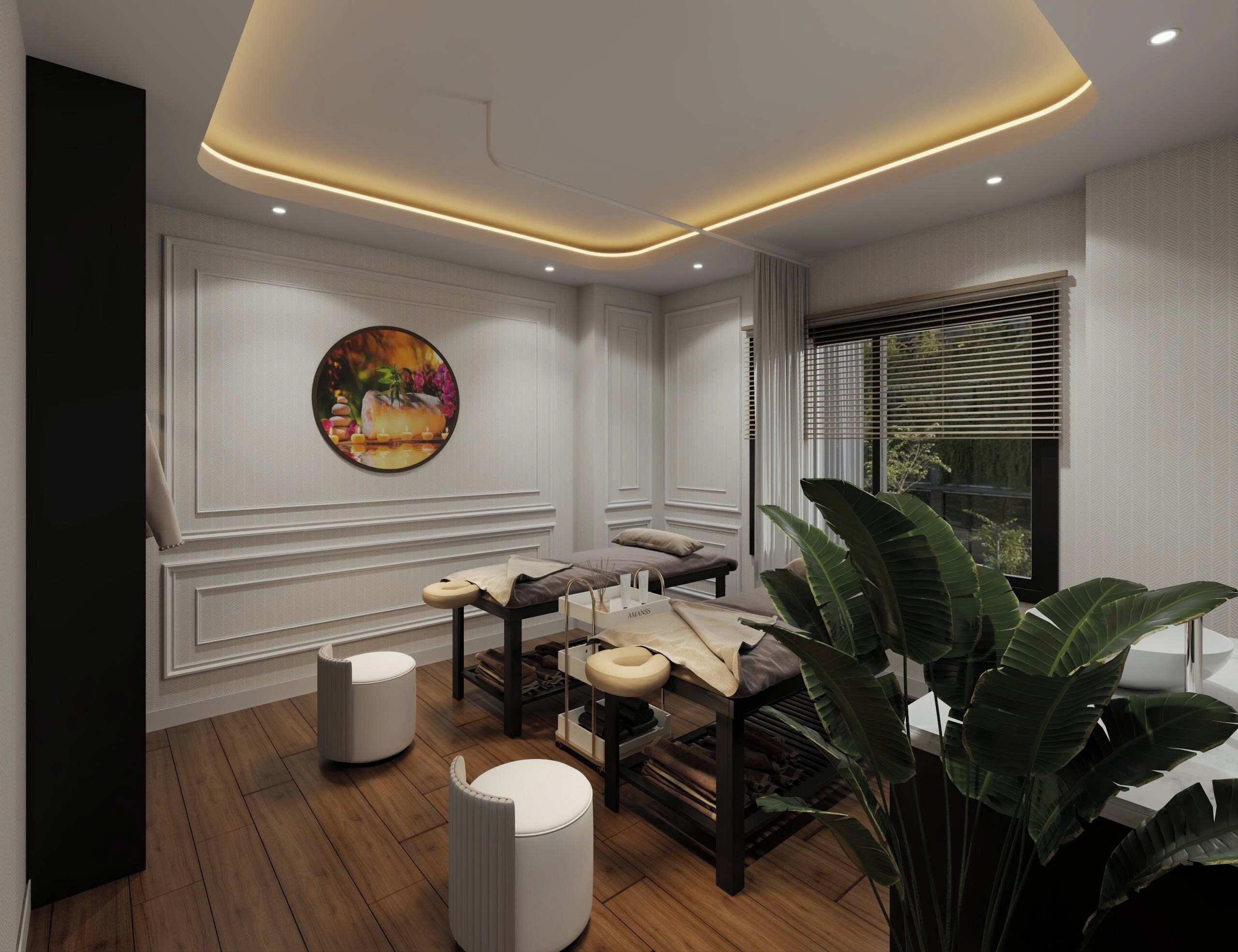 A modern spa room with a wooden floor, a massage table, a large plant, and a wall-mounted artwork.