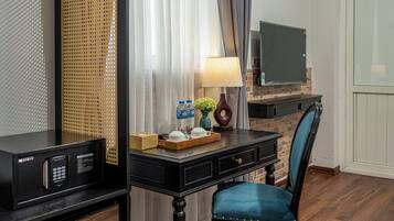 A hotel room with a desk, a chair, a television, a lamp, and a window with curtains.