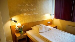 Ett hotellrum med en säng, sängbord, ett litet bord med en lampa och en vägg med texten ”God natt” på flera språk.