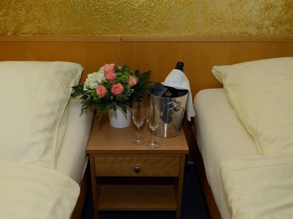 Habitación de hotel con dos camas, una mesita de noche de madera con un florero y dos copas de champán, además de una botella de champán.