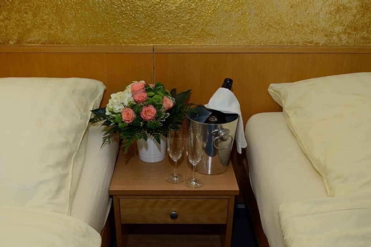 Habitación de hotel con dos camas, una mesita de noche de madera con un florero y dos copas de champán, además de una botella de champán.