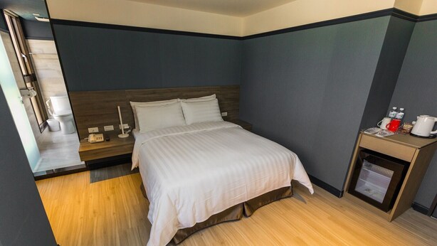 A hotel room with a bed, bedside table, and a small desk with a coffee maker. - Queen Hotel (Kaohsiung)