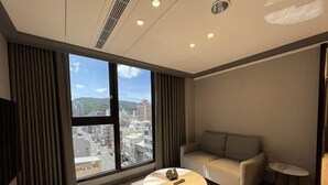 A modern hotel room with a large window, a round coffee table, a sofa, and a small side table. - Queen Hotel (Kaohsiung)