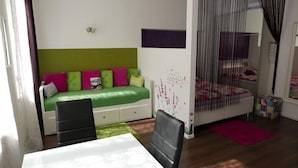 A bedroom with a green sofa, a bed with a purple headboard, a desk, and a chair. - Govienna Small Modern Apartment (Vienna)