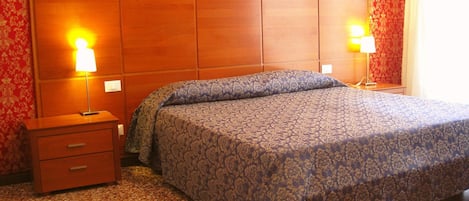 A hotel room with a large bed, wooden headboard, two bedside tables with lamps, and a carpeted floor.