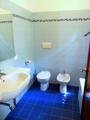 A bathroom with a sink, toilet, and bidet, tiled in light blue and white, with a blue floor. - Maison De Charme Balbi (Venice)