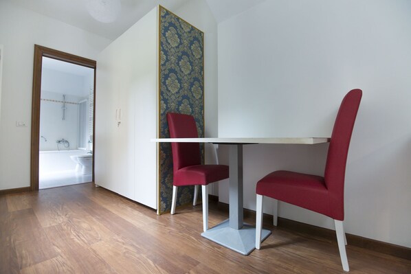 A room with a white table and two red chairs, a wooden floor, and a bathroom visible through an open door. - Maison De Charme Balbi (Venice)
