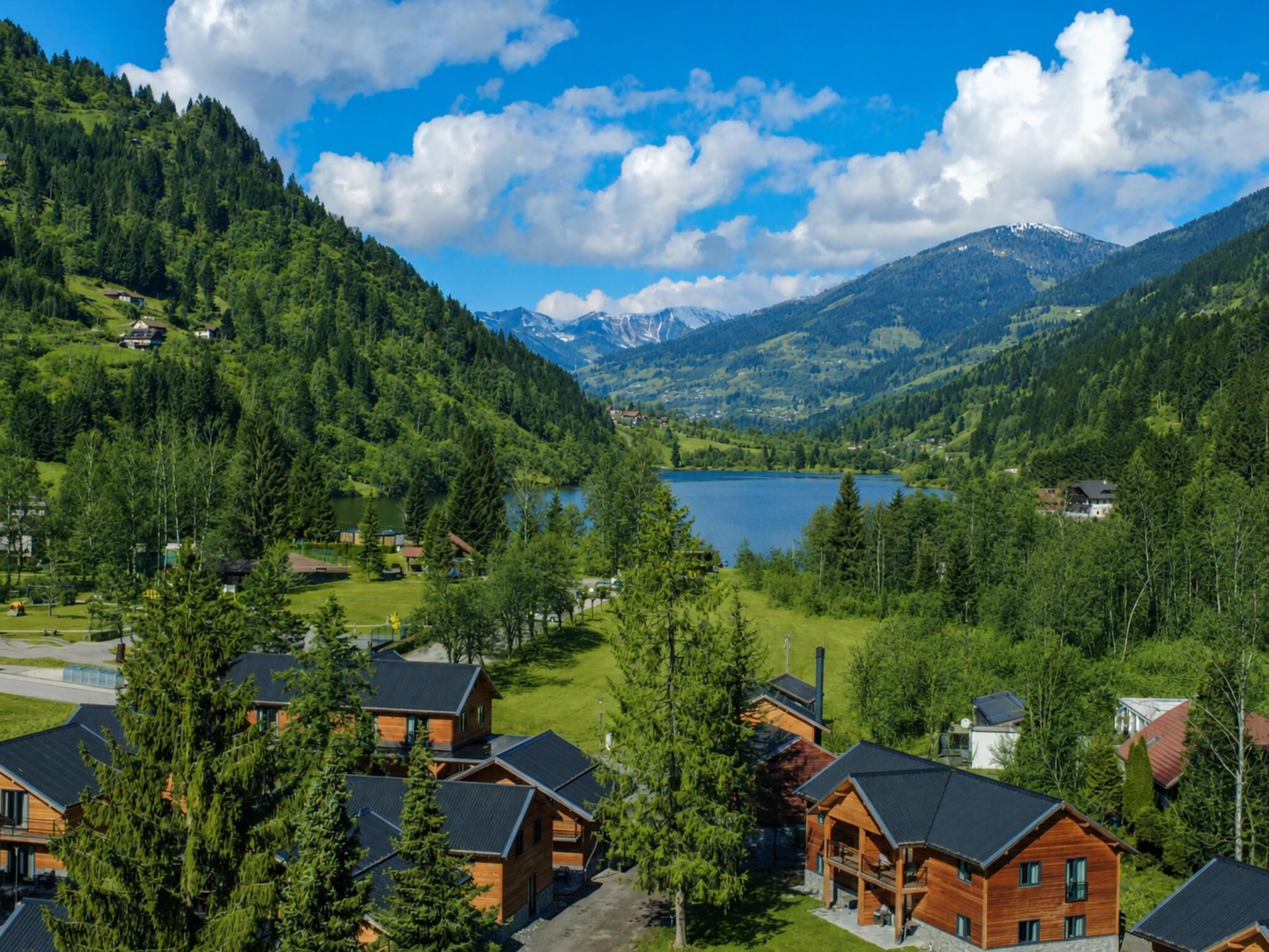 A mountainous landscape with a lake, surrounded by forested areas and wooden cabins.