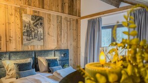 A bedroom with a wooden wall, a bed with multiple pillows, a nightstand, and a window with curtains. - Chalet with terrace and sauna on an Alpine lake (Afritz am See)