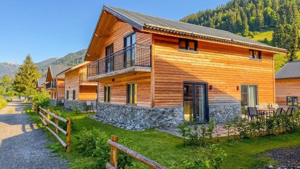 A wooden cabin with a balcony, stone foundation, and a view of the surrounding forest. - Chalet with terrace and sauna on an Alpine lake (Afritz am See)