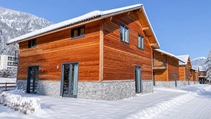 A wooden cabin with a stone foundation, a balcony, and a snow-covered landscape. - Chalet with terrace and sauna on an Alpine lake (Afritz am See)