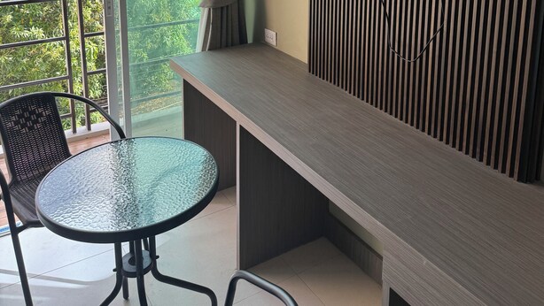 A modern room with a balcony, a TV mounted on the wall, a dining table with chairs, and a view of buildings and greenery outside. - Sitara Hotel Patong Beach (Patong)