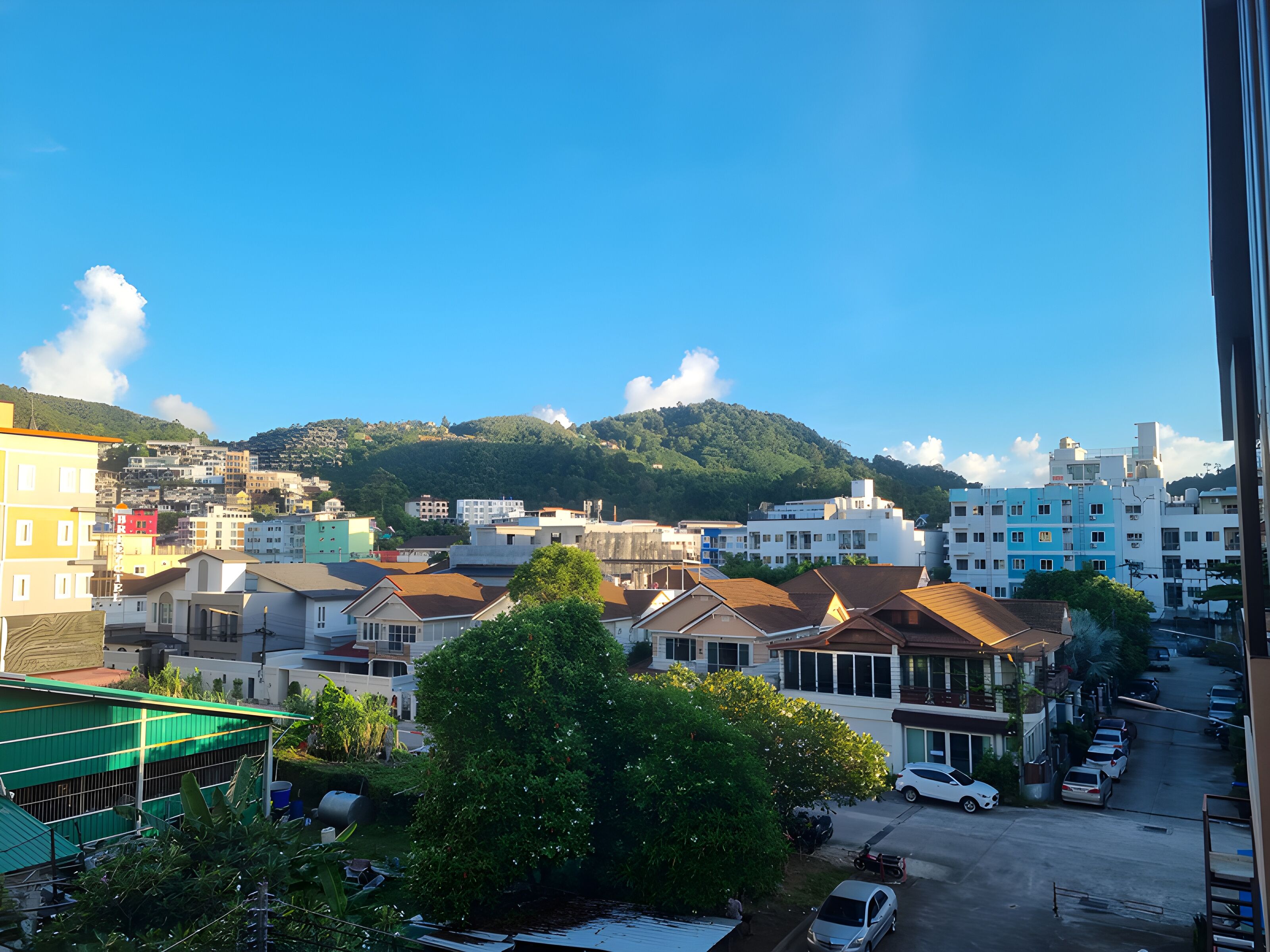 A residential area with houses, parked cars, and a hill in the background.