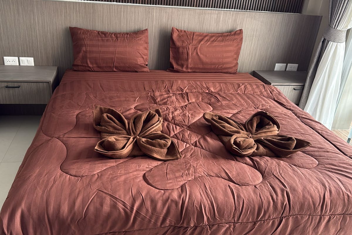 A neatly made bed with a large, textured bedspread and two decorative towels arranged in a bow shape.