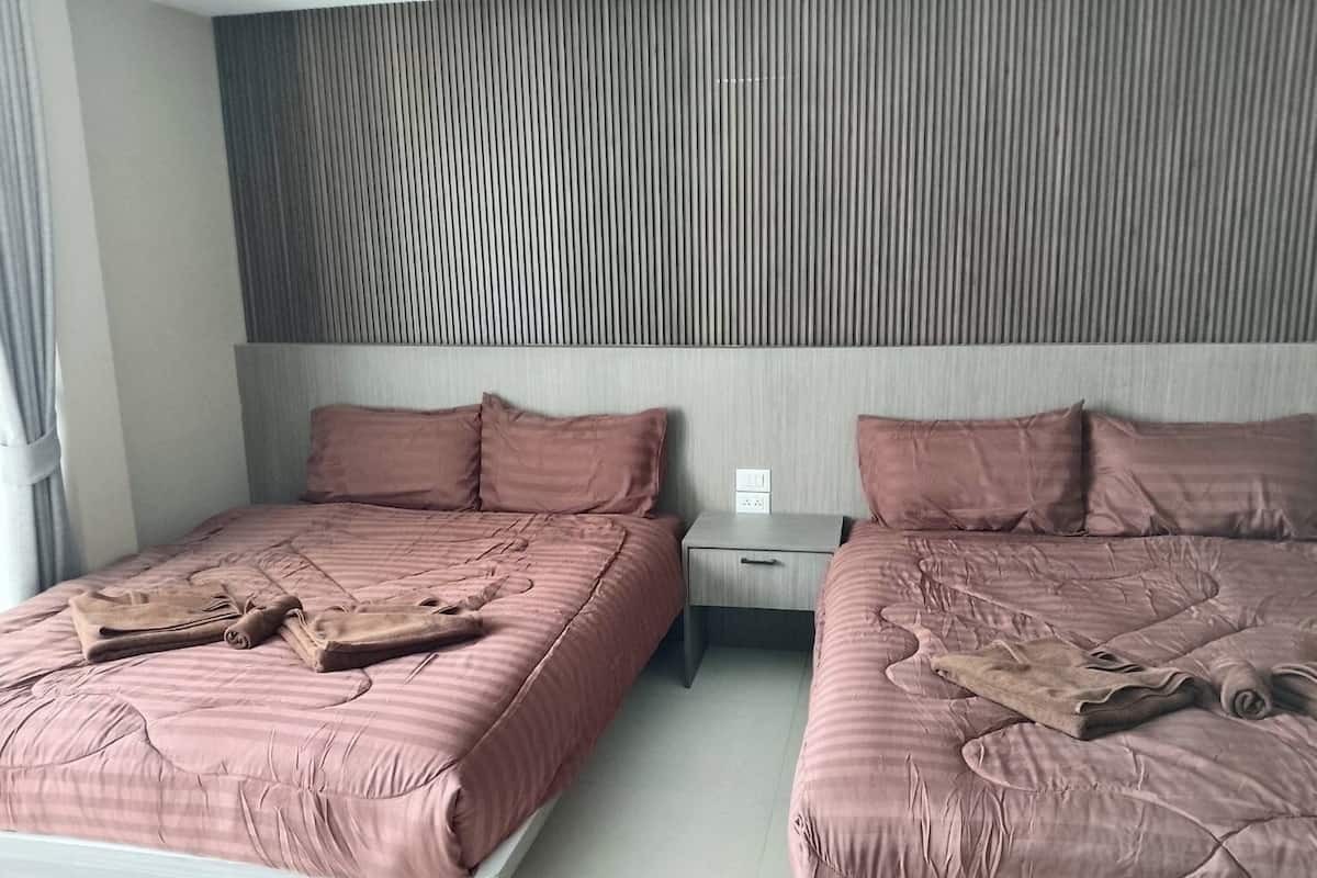 A hotel room with two beds, each with a pink bedspread and matching pillows. There is a nightstand between the beds with a drawer and a power outlet.