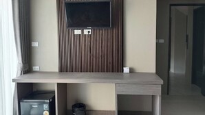 A modern hotel room with a flat-screen TV mounted on a wooden panel wall, a small minibar, and a trash bin. - Sitara Hotel Patong Beach (Patong)