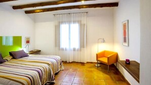 Een kamer met twee bedden, een stoel, een raam met gordijnen en een lamp.