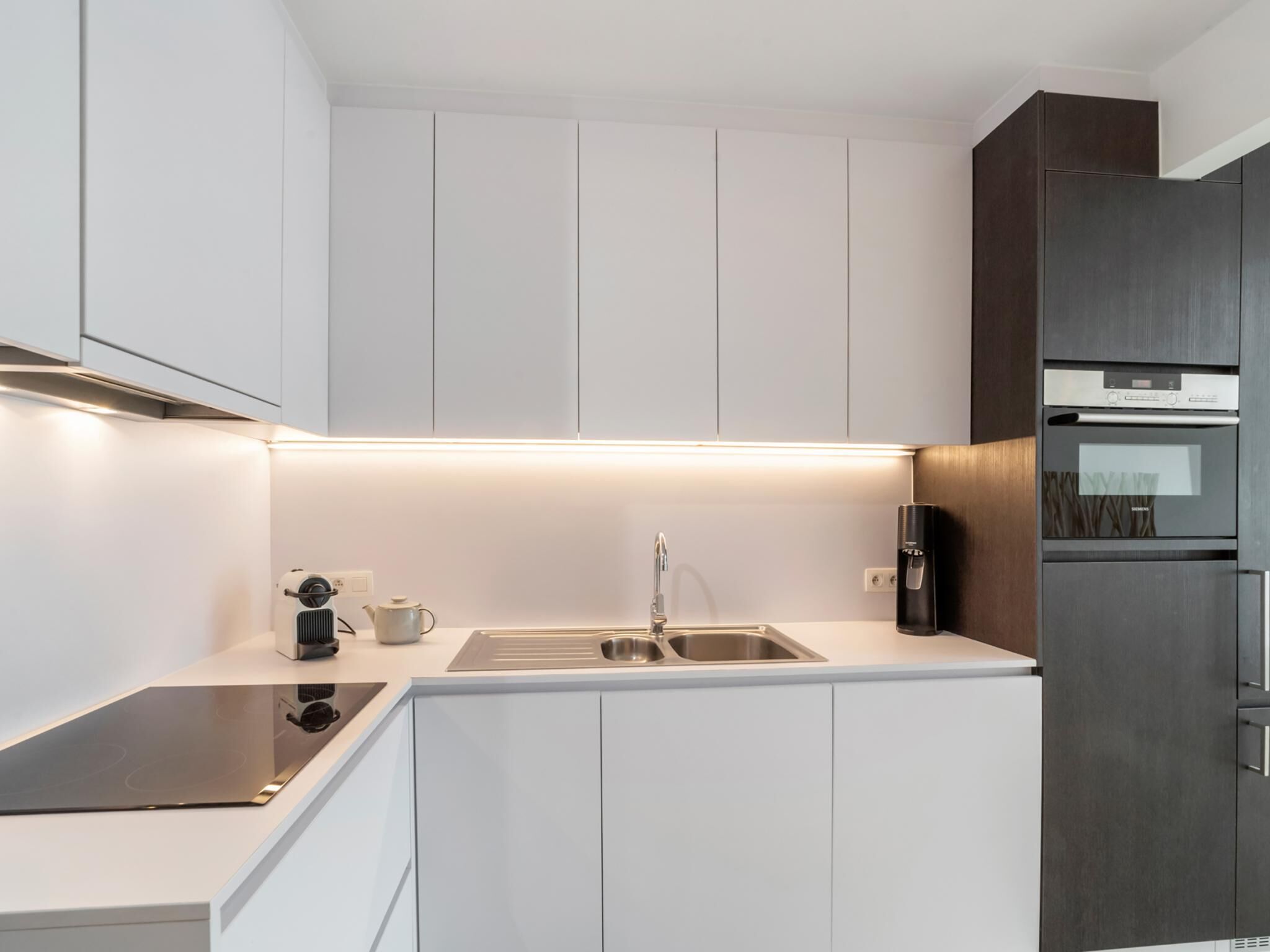 Een moderne keuken met witte kastjes, een roestvrijstalen spoelbak, een ingebouwde oven en een koffiezetapparaat.