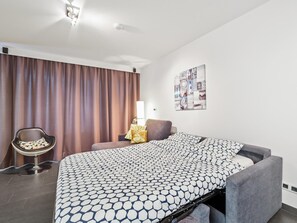 A hotel room with a bed, a chair, a desk, and a wall-mounted lamp. - Spacious studio with sea view (Blankenberge)