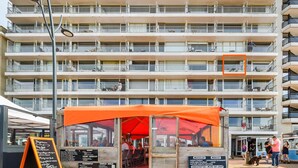 Ein mehrstöckiges Hotel mit Balkonen, ein Restaurant im Erdgeschoss mit einer orangefarbenen Markise und ein sichtbares Schild mit Text.
