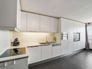 A modern kitchen with white cabinets, a built-in oven, and a dishwasher. - Spacious studio with sea view (Blankenberge)