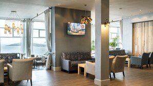 A modern hotel lobby with a seating area, wooden flooring, and a large window offering a view of the sea. - Fistral Beach Hotel And Spa Adults Only (Newquay)