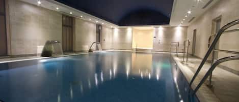 A large indoor swimming pool with a starry ceiling, surrounded by walls with a light-colored tile pattern.