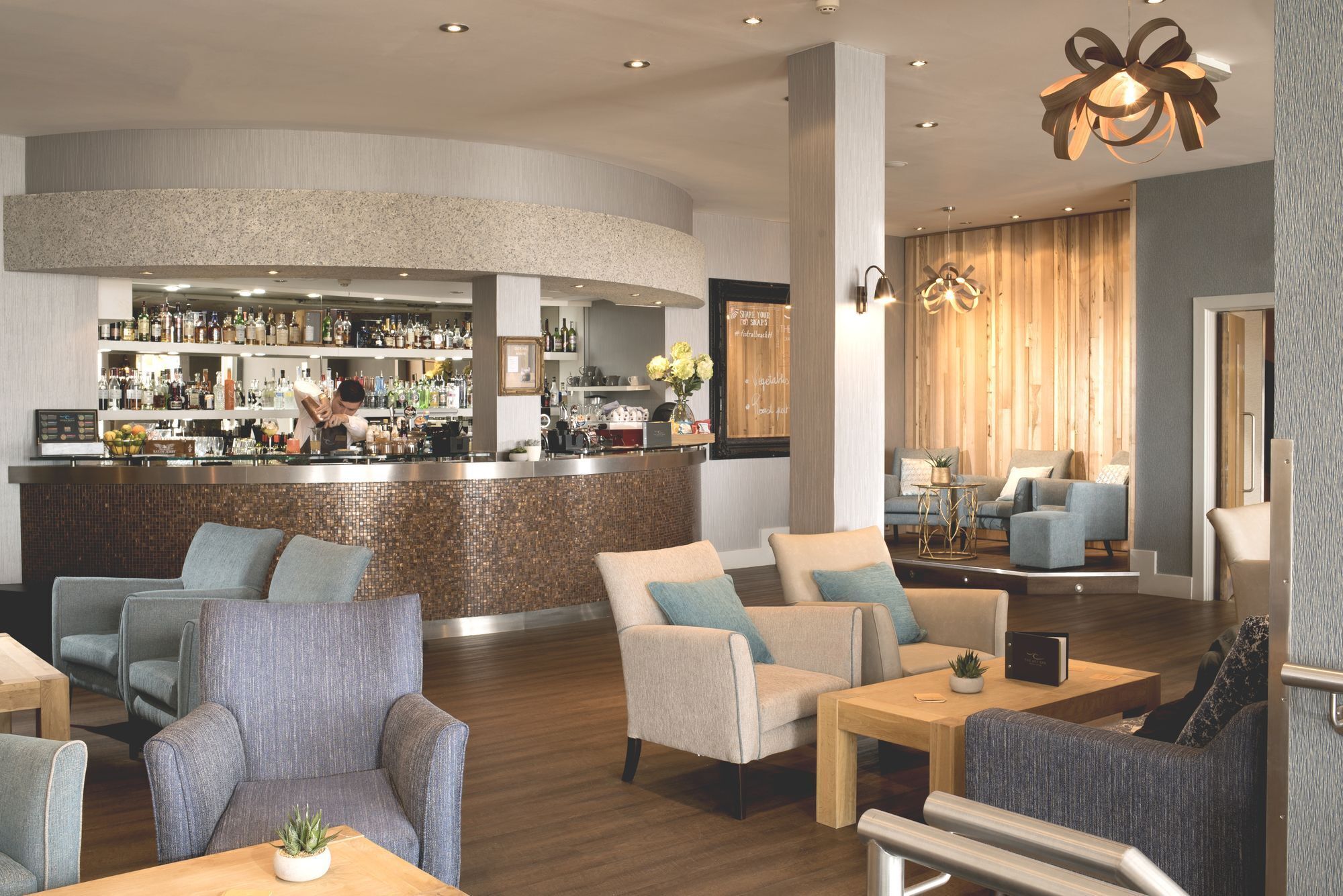 A modern bar area with a curved counter, bar stools, and a seating area with sofas and armchairs.