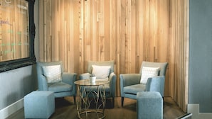 A cozy seating area with two armchairs and a small round table, set against a wooden wall with a decorative light fixture above. - Fistral Beach Hotel And Spa Adults Only (Newquay)