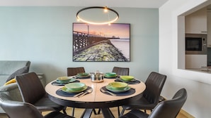 Un coin repas avec une table ronde, des chaises noires et un tableau représentant une jetée accroché au mur.