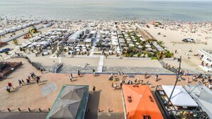 Une zone située au bord de la plage, avec plusieurs parasols, des chaises longues et quelques personnes qui se promènent.