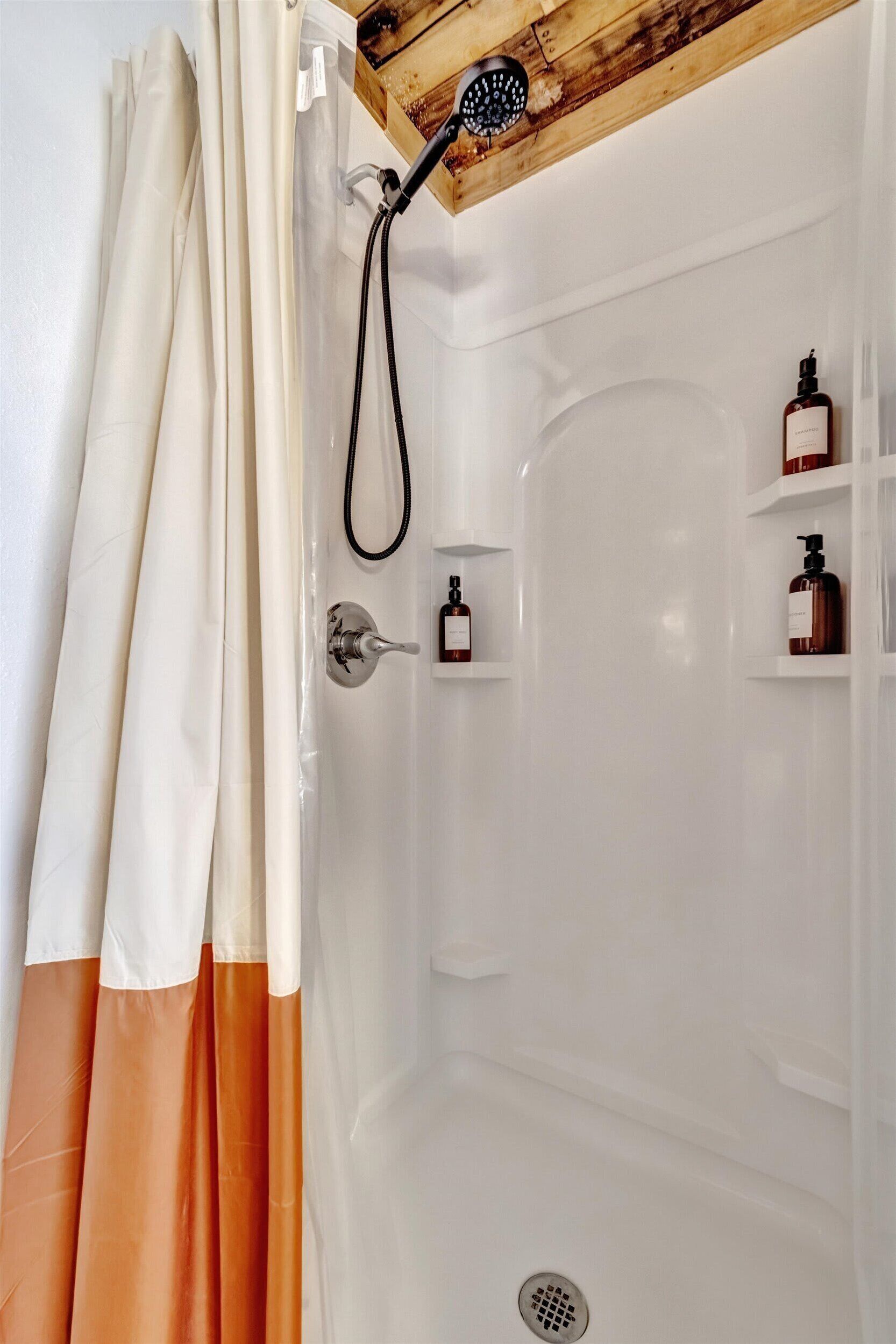 A shower area with a wooden ceiling, a showerhead, and two shelves with bottles.