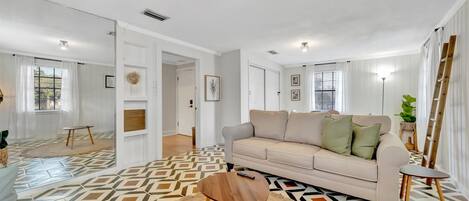 Una sala moderna con un sofá color beige, una mesa redonda de madera y piso estampado.