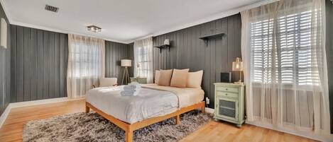 Un dormitorio con una cama grande, suelo de madera, paredes grises y una mesita de noche verde.