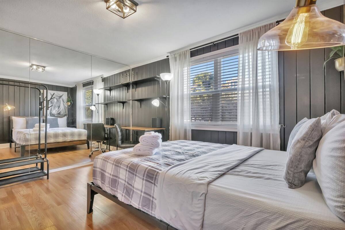 A modern bedroom with a large bed, a desk, and a mirror.