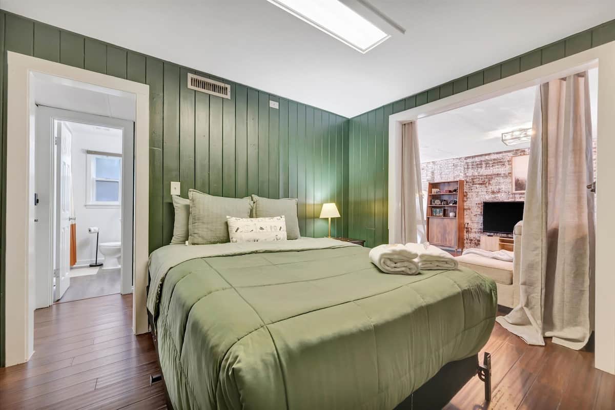 A bedroom with a bed, a bedside lamp, a TV, and a window with curtains.