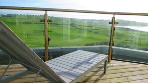 Un balcon doté d’une terrasse en bois, d’une rambarde en métal et offrant une vue sur un paysage verdoyant.