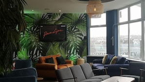 Un salon moderne doté d’un grand téléviseur, de sièges confortables et de grandes fenêtres offrant une vue sur la ville.