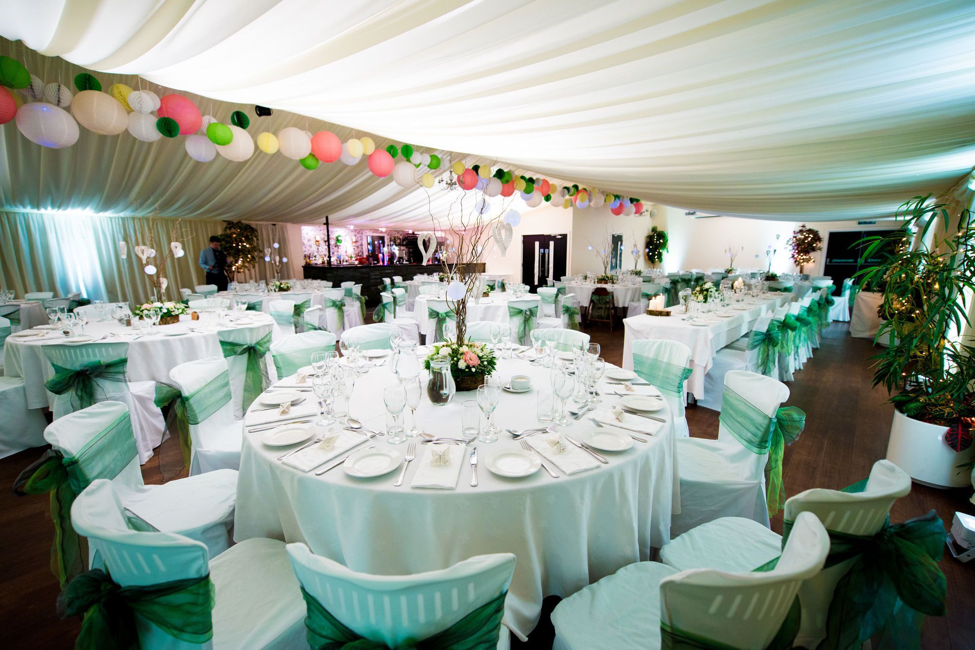 A banquet hall with round tables set for dining, white tablecloths, and green chair covers.
