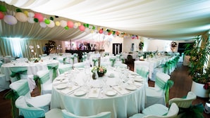 Une salle de banquet avec des tables rondes dressées pour le repas, des nappes blanches et des housses de chaise vertes.