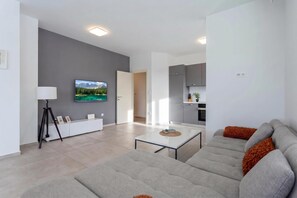 A modern living room with a sofa, a coffee table, and a TV mounted on the wall. - Apartment Sang Near The Beach (Pula)