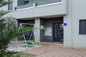 Ein modernes Gebäude mit grauer Fassade, einer Schaukel und einer Tür mit einem Schild, das eine 5-Sterne-Bewertung anzeigt.