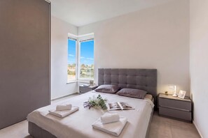 A modern bedroom with a large bed, a nightstand, a window with a view, and a bedside table with a lamp. - Apartment Sang Near The Beach (Pula)