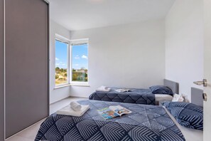 Ein Schlafzimmer mit zwei Betten, einem großen Fenster und Blick ins Freie.