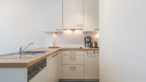 Uma cozinha moderna com armários brancos, uma pia de aço inoxidável e uma cafeteira.